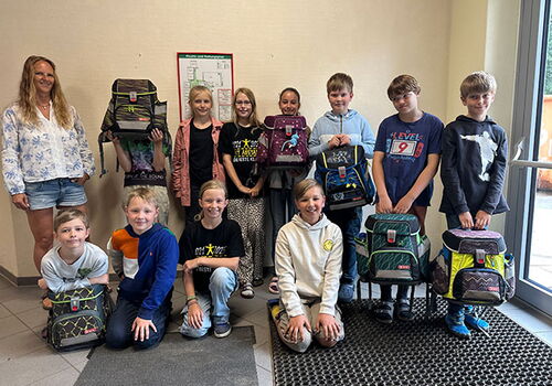 Schulkinder mit Rucksäcken posieren für ein Gruppenfoto.