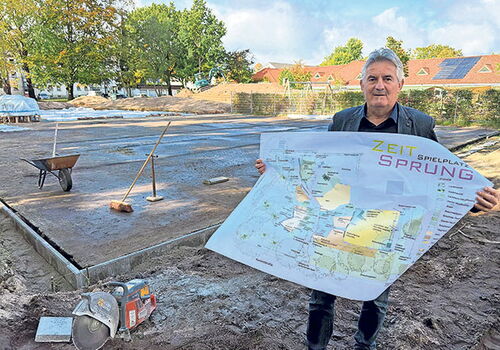 Mann mit Plan vor Baustelle eines Spielplatzes.