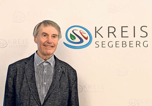 Mann steht vor einer Wand mit Kreis Segeberg Logo.