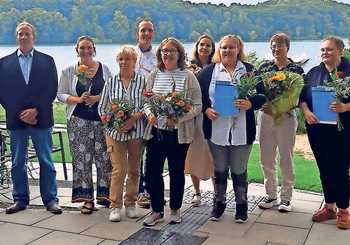 Gruppe von Menschen mit Blumen vor einem See.