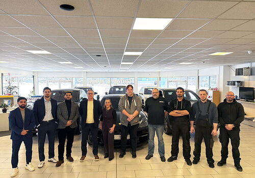 Team in einem Autohaus steht in einer Reihe vor Fahrzeugen.