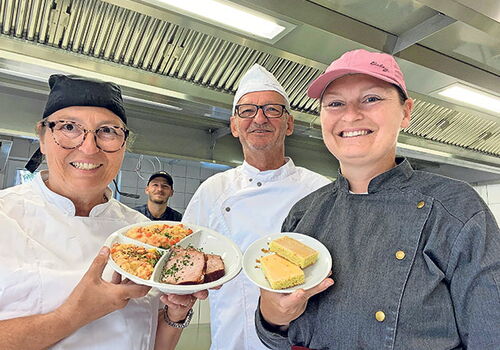 Küchenteam präsentiert Teller mit verschiedenen Gerichten.