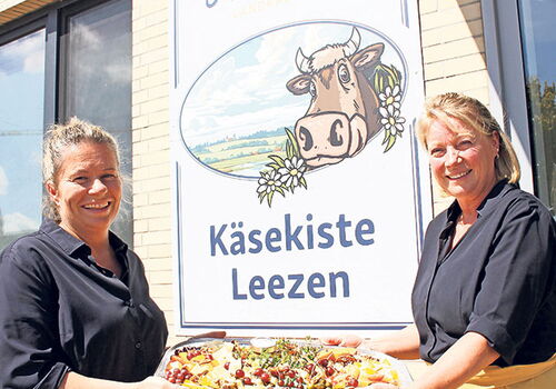 Zwei Frauen präsentieren eine Käseplatte vor einer Käserei.