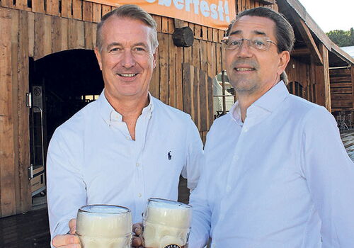 Zwei Männer mit Bierkrügen vor Oktoberfest-Dekor.