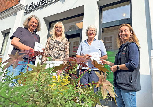 Vier Personen vor einer Apotheke mit Pflanzen im Vordergrund.
