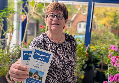 Frau mit Brille hält Broschüren im Wintergarten.
