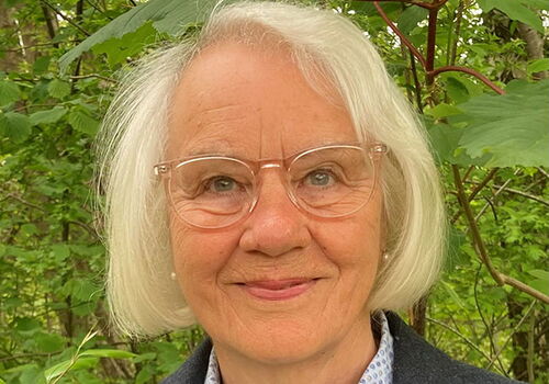 Ältere Frau mit Brille vor grünen Blättern