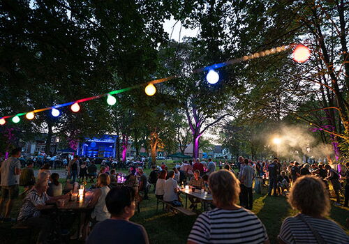 Menschen feiern bei einem bunten Fest im Park am Abend.