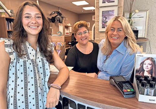 Drei Frauen stehen lächelnd an einem Tresen im Friseursalon.