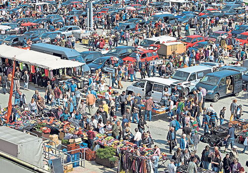 Menschenmengen auf einem belebten Flohmarkt mit vielen Autos.