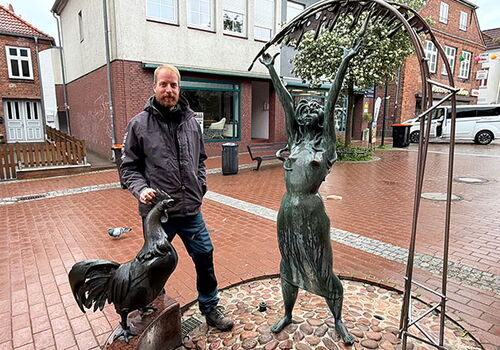 Mann steht neben Bronzeskulpturen auf einer regennassen Straße.