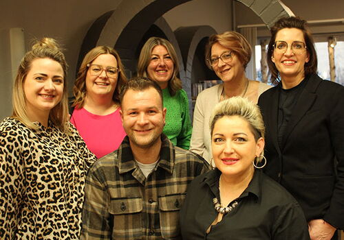 Gruppe von sieben lächelnden Menschen in einem Büro.