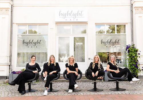 Fünf Frauen sitzen vor einem Friseursalon auf Drehstühlen.