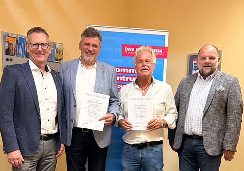 Vier Männer posieren mit Urkunden vor einem Banner.