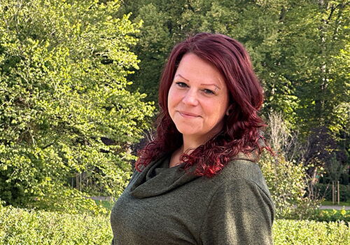 Frau im Freien vor einem grünen Hintergrund lächelt.