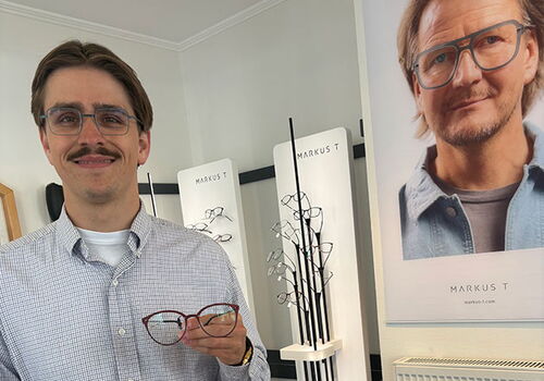 Mann hält Brille in Optiker-Geschäft mit Plakaten.
