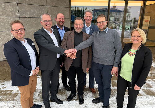 Acht lächelnde Personen stehen vor einem Gebäude.