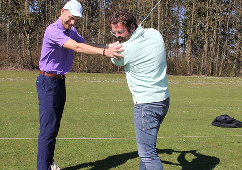 Zwei Männer beim Golftraining auf einem Rasenplatz.