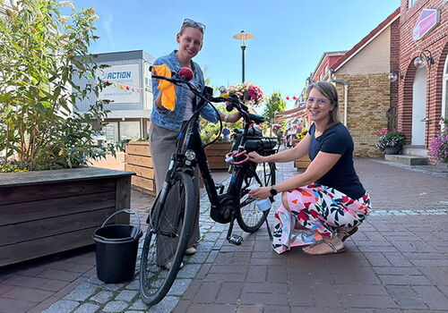 Zwei Frauen reinigen Fahrräder auf gepflasterter Straße.