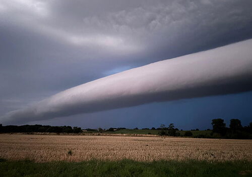 Langer Wolkenstreifen am Himmel über einem Feld bei Gewitter.