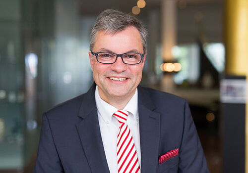 Mann in Anzug mit rot-weiß gestreifter Krawatte lächelt.