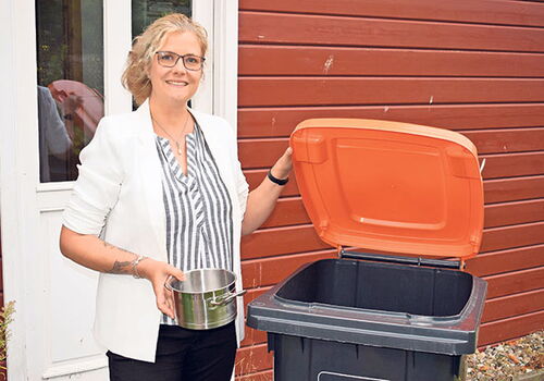 Frau hält Kochtopf, steht vor Mülltonne mit offenem Deckel.
