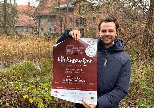 Mann hält Plakat für Winterzauber-Markt in der Hand.