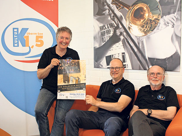 Kulturveranstaltungsposter vom Team präsentiert. Drei Personen mit Kulturposter auf einem Sofa.