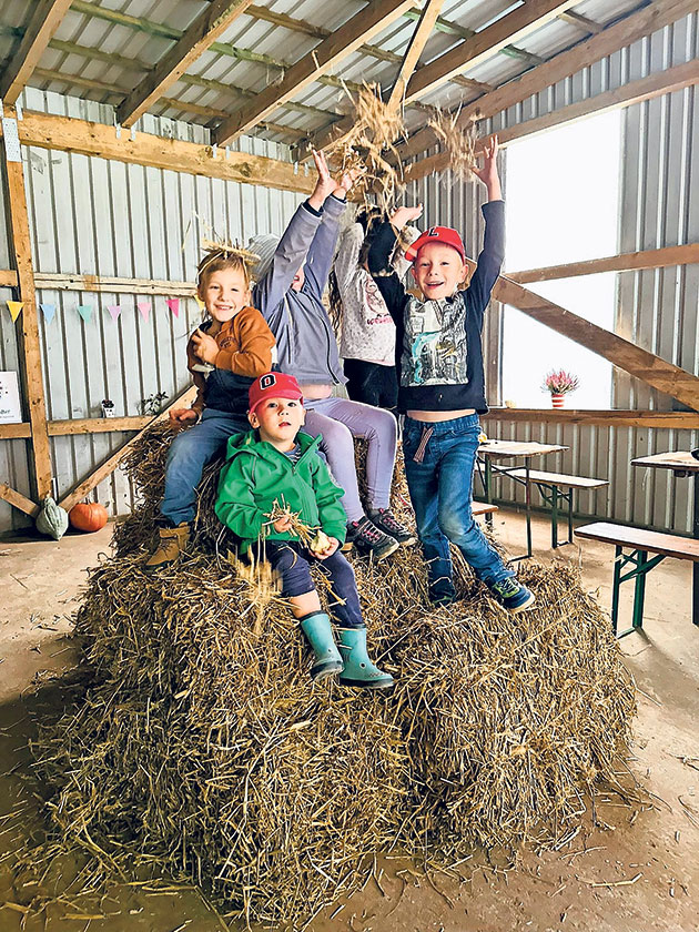 Kinder spielen auf einem Strohballen im Scheuneninnenraum.