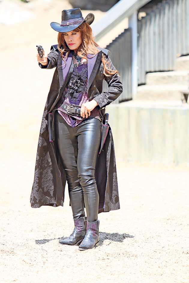 Frau im Cowboy-Outfit mit Hut hält Revolver im Anschlag.