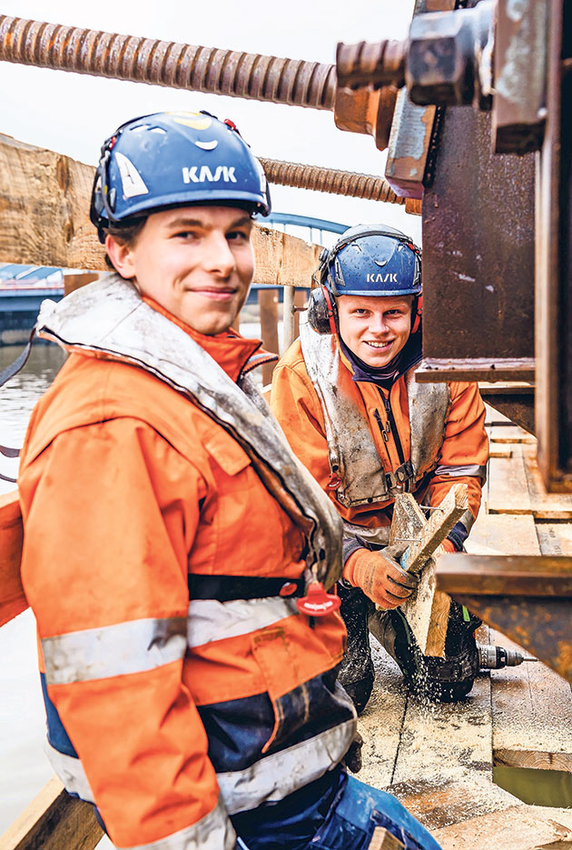 Arbeiter auf Baustelle am Wasser in Schutzkleidung Zwei Arbeiter in Schutzkleidung auf einer Baustelle am Wasser.