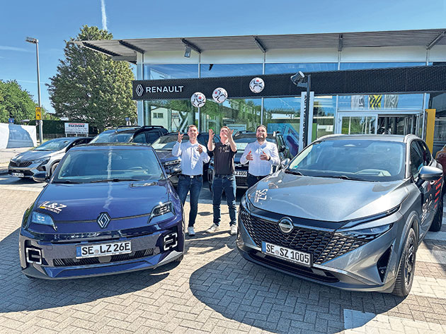 Personen posieren mit Renault-Autos vor einem Showroom. Drei Personen vor Renault-Autos vor einem Autohaus.