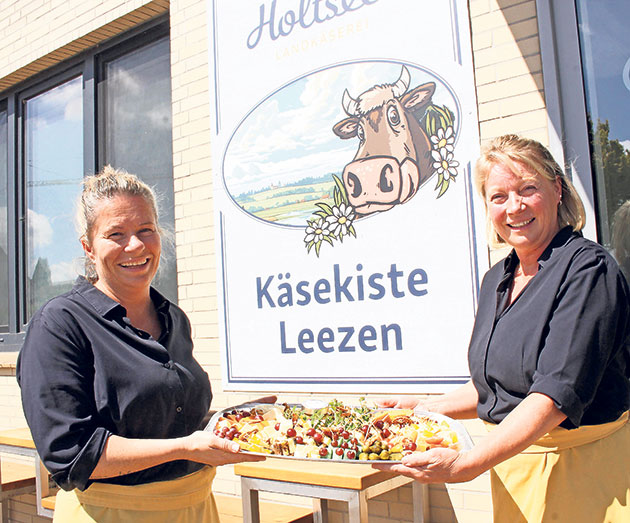 Käsekiste Leezen: Leckere Käseplatten genießen Zwei Frauen halten eine Käseplatte vor der Käsekiste Leezen.