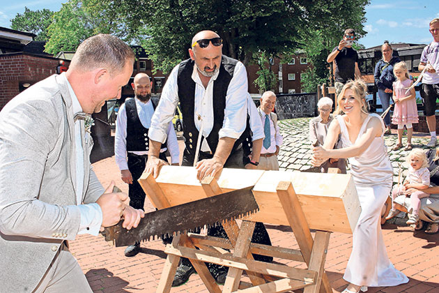 Traditioneller Holzschnitt bei einer Hochzeit Brautpaar sägt gemeinsam ein Holzstück durch.