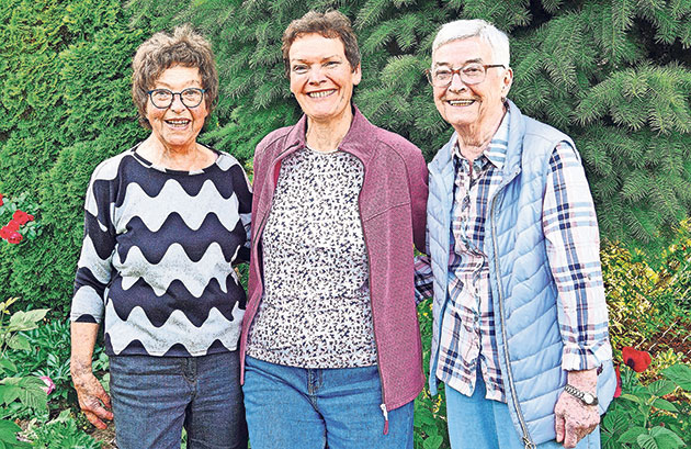 Drei lächelnde Frauen stehen in einem Garten.
