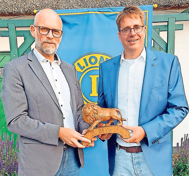 Männer präsentieren eine Löwenfigur aus Holz. Zwei Männer halten eine Holzfigur eines Löwen.