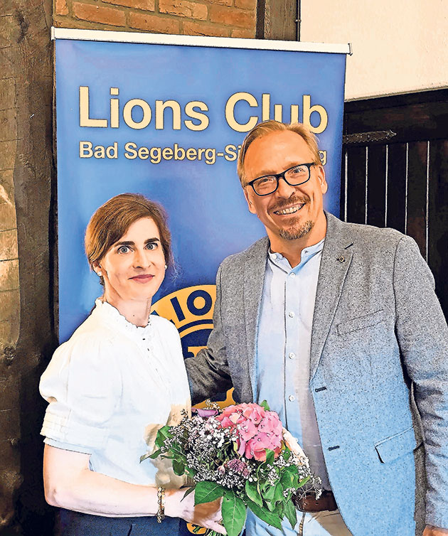 Zwei Personen vor einem Lions Club-Banner mit Blumenstrauß.