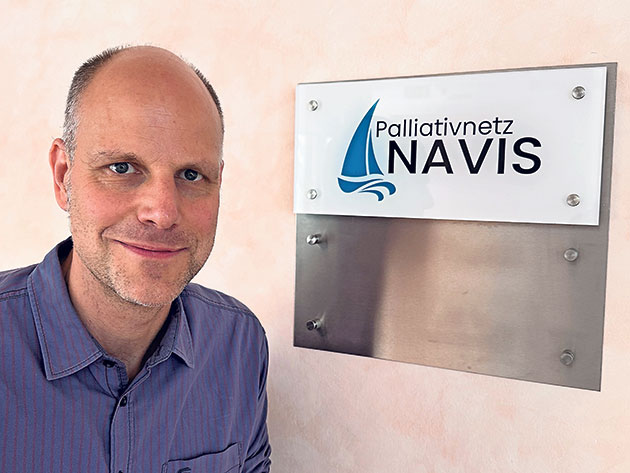 Palliativnetz NAVIS Schild mit Mann Mann neben Palliativnetz NAVIS Schild