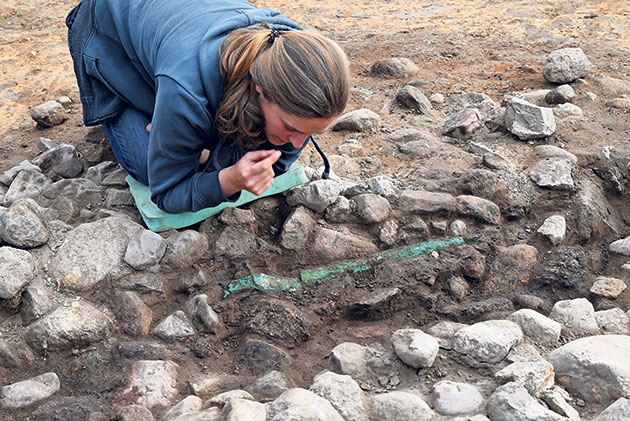 Frau untersucht archäologische Fundstelle mit Steinen.