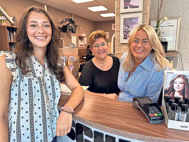 Drei Frauen stehen lächelnd an einem Tresen im Friseursalon.