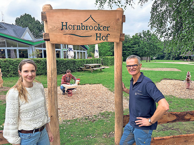 Eingang zum Hornbrooker Hof mit zwei Personen Zwei Personen vor dem Schild 'Hornbrooker Hof'.