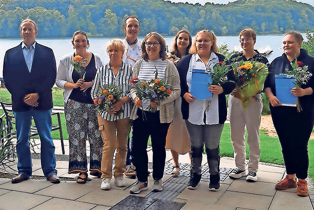 Gruppe von Menschen mit Blumen vor einem See.