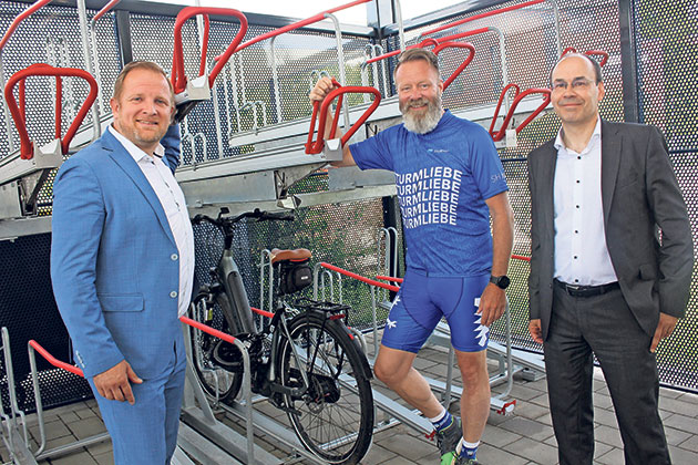 Drei Männer posieren neben einem Fahrradständer.