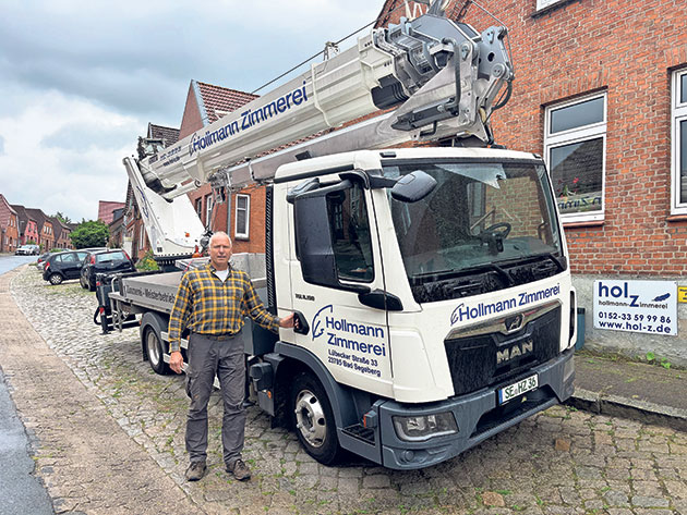 LKW mit Kran vor einem Gebäude geparkt Mann steht neben einem LKW mit einem Kran bei einem Gebäude.