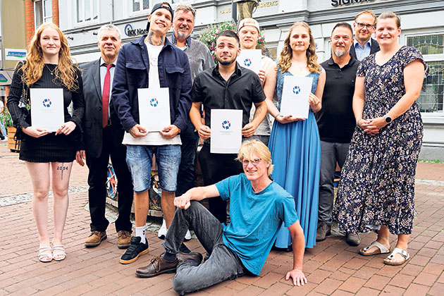 Gruppenfoto mit Urkunden auf der Straße. Gruppe von Menschen posiert auf Pflastersteinen mit Urkunden.