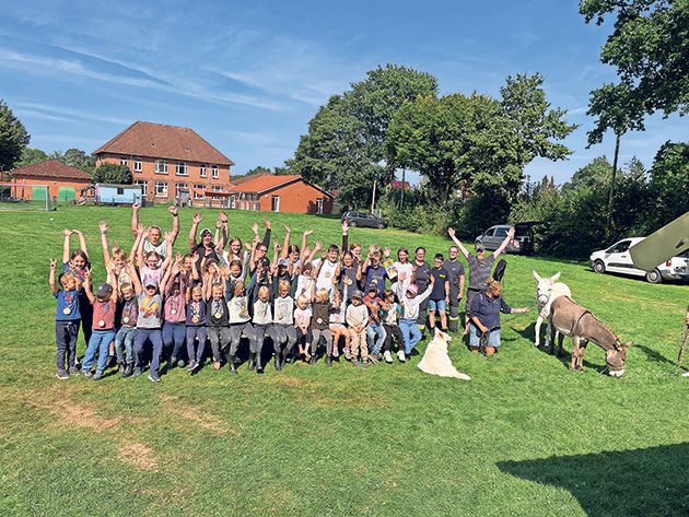 Kindergruppe auf Wiese mit Tieren und erhobenen Armen