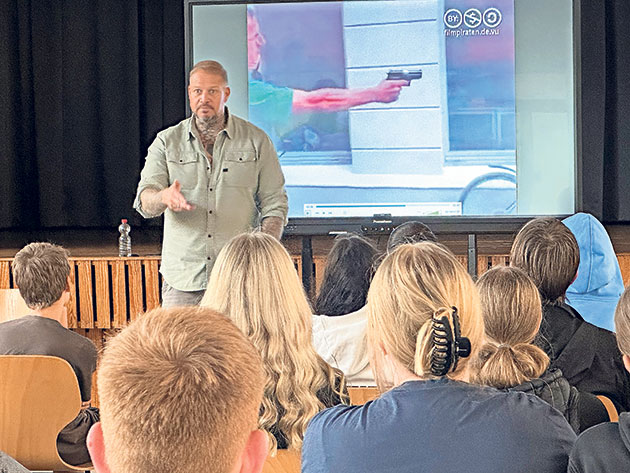 Vortrag über Gewaltprävention in der Schule Mann hält Vortrag vor Schülern mit Bild von Waffe auf Bildschirm.