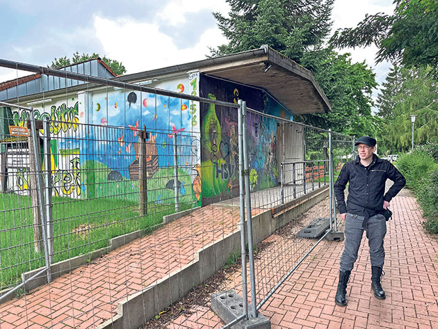Buntes Gebäude mit Grafitti hinter einem Bauzaun Mann neben einem bunt bemalten Gebäude hinter einem Zaun.