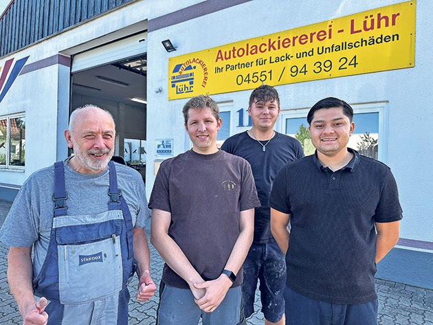 Autolackiererei Lühr Team vor dem Geschäft Vier Männer stehen vor einer Autolackiererei.