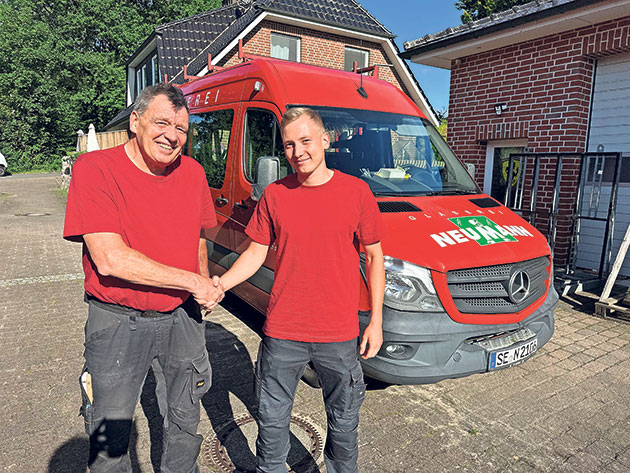 Kollegen begrüßen sich vor Firmenfahrzeug Zwei Männer schütteln Hände vor einem roten Lieferwagen.